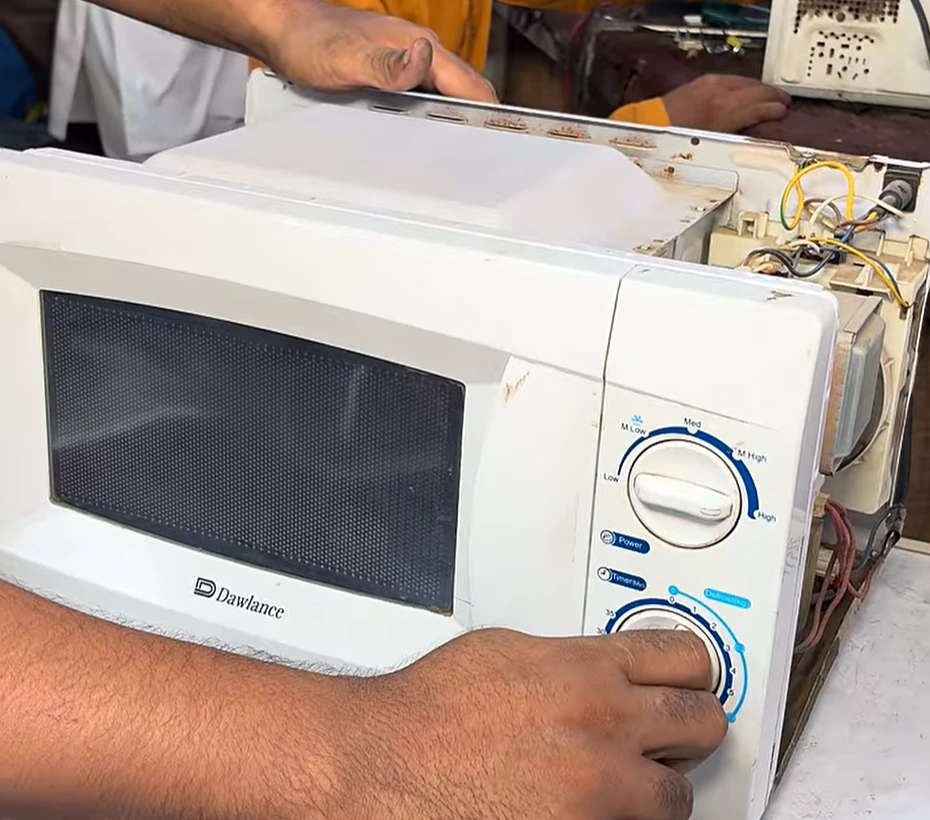 Dawlance microwave oven opened for repair while a technician tests the control dial